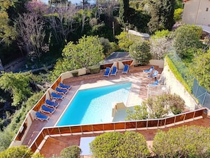 A swimming pool with blue lounge chairs, surrounded by greenery and a fenced area.