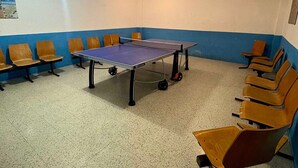 Une table de ping-pong dans une pièce aux murs bleus et blancs, entourée de chaises en bois.