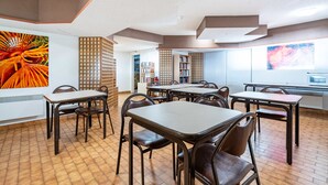 Un espace repas avec des tables et des chaises, une bibliothèque et une grande fenêtre.