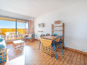 Un balcon avec une table et des chaises en bois, un canapé et un téléviseur fixé au mur.