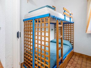 A bunk bed with a wooden frame and blue accents, a white wall, and a tiled floor.