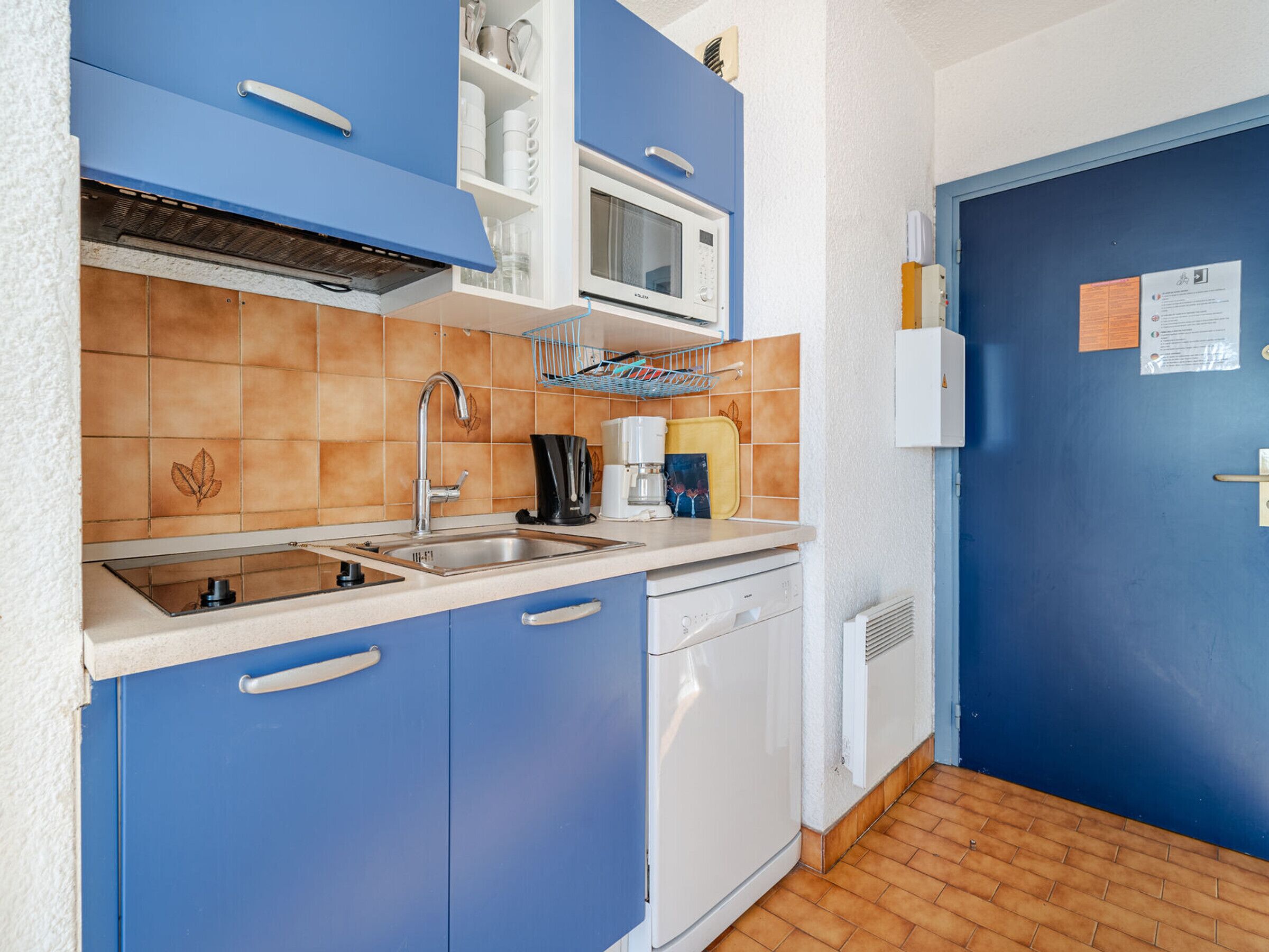 Una cocina compacta con armarios azules, un lavavajillas blanco y un microondas.