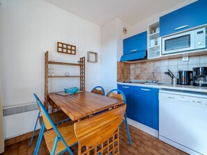 A compact kitchen with blue cabinets, a wooden dining table, and a microwave.