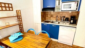 A compact kitchen with blue cabinets, a microwave, a sink, and a wooden dining table with chairs. - Apartment for 8, sea view, Wi-Fi included (Roquebrune-Cap-Martin)