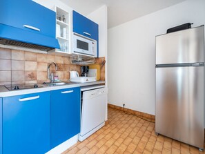A modern kitchen with blue cabinets, a stainless steel refrigerator, a microwave, and a dishwasher.
