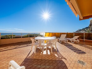 A sunlit outdoor patio with a round table and white chairs, overlooking a coastal view.