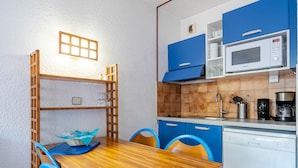 A compact kitchen with a wooden table, blue chairs, a microwave, and a coffee maker. - Apartment 8 people, Wi-Fi, sea view (Roquebrune-Cap-Martin)