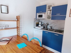 Una cocina compacta con armarios azules, microondas, cafetera y pileta.