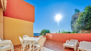 Une terrasse avec une table et des chaises, une vue sur la mer et un mur en pierre.