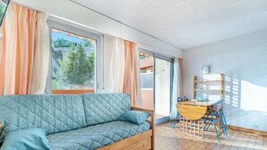 Une pièce chaleureuse avec un canapé en bois, une table à manger avec des chaises et de grandes fenêtres dotées de rideaux.