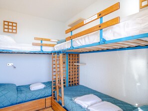 A bunk bed room with wooden frames and blue accents, featuring a small window and a wall-mounted shelf.