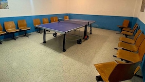 A ping pong table in a room with blue and white walls, surrounded by wooden chairs.