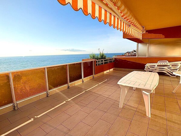Una terraza con vista al mar, una mesa, sillas y una barandilla.