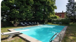 A rectangular swimming pool with a diving board and a ladder, surrounded by grass and trees. - Romantic bedroom in +600years old villa, with pool view (Grassina)