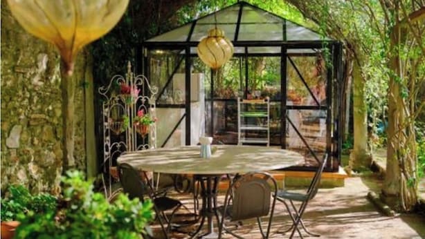 A greenhouse with a glass roof, a round table, and chairs in a garden setting. - Romantic bedroom in +600years old villa, with pool view (Grassina)