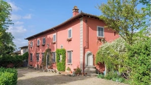 A pink villa with a gravel driveway, surrounded by greenery and potted plants. - Romantic bedroom in +600years old villa, with pool view (Grassina)