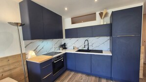Una cocina moderna con armarios azul oscuro, un salpicadero de mármol y un horno empotrado.
