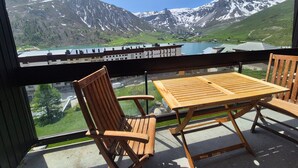 Un balcón con mesa y sillas de madera, que ofrece vistas a montañas nevadas y un lago.