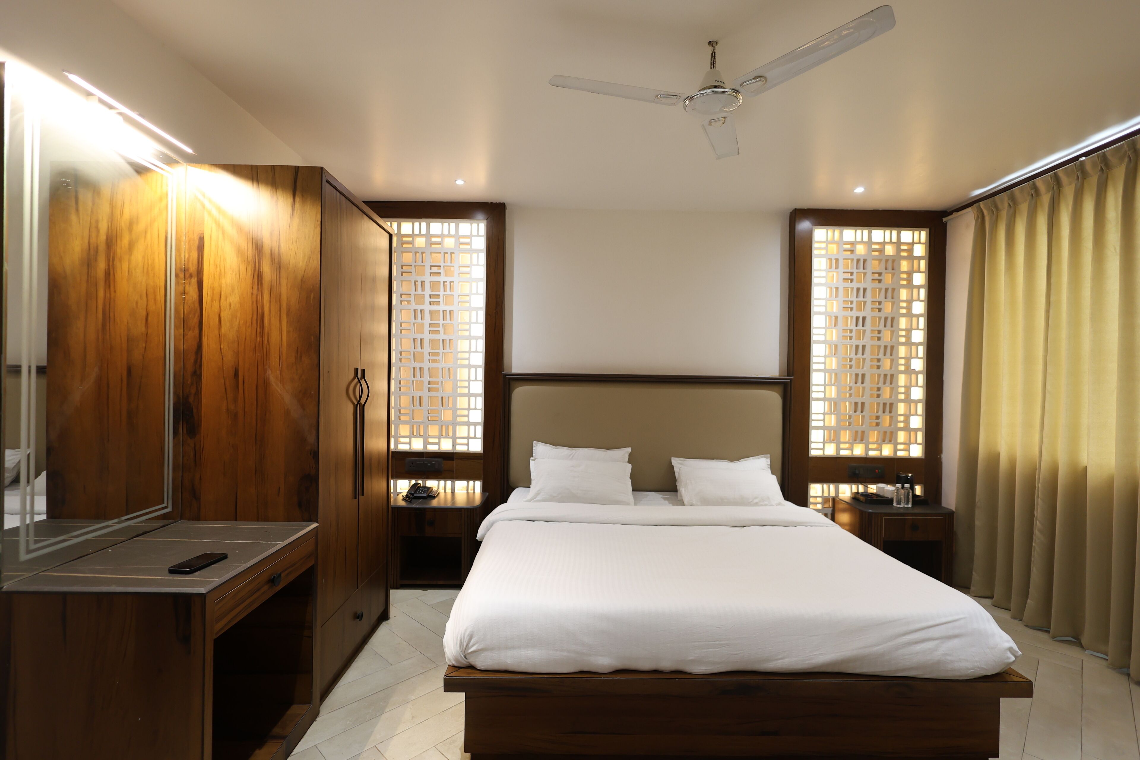 Une chambre d’hôtel avec un grand lit, une armoire en bois, des tables de chevet et un ventilateur de plafond.