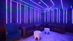 A modern lounge area with a blue armchair, a tufted leather sofa, and two white side tables. - Vasuh Mhangglam (Bilha)