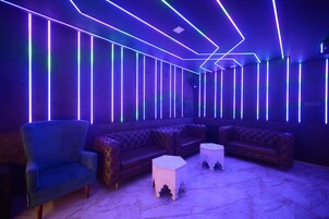 Un espacio lounge moderno con un sillón azul, un sofá de cuero capitonado y dos mesitas blancas.