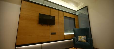 A modern room with a wooden panel wall, a flat-screen TV, and a teal armchair.