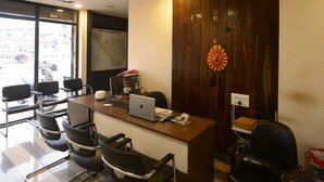 A conference room with a wooden desk, black office chairs, a ceiling fan, and a window with a view of buildings. - Vasuh Mhangglam (Bilha)