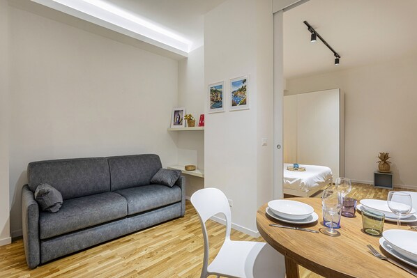 A modern living room with a grey sofa, a dining table set with plates and glasses, and a wooden floor.