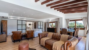 Een ruime woonkamer met een bruine leren bank, houten vloeren en een eethoek met een tafel en stoelen.