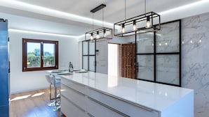 Een moderne keuken met een groot eiland, hanglampen en uitzicht door een glazen deur.