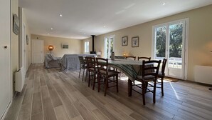 Un comedor amplio con una mesa larga y sillas, una chimenea y ventanas grandes que ofrecen vistas al exterior.