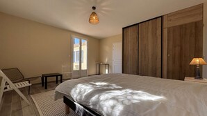 Un dormitorio con una cama grande, un armario de madera, una mesita y una silla.