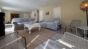 Amplia sala de estar con dos sofás, una mesa de centro y un sillón de mimbre.