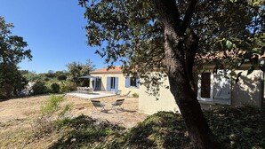 Una casa con un patio, mobiliario exterior y un árbol al frente.