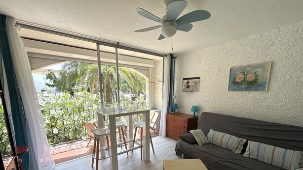 Una sala de estar con sofá, una mesita, ventilador de techo y balcón con sillas y una mesa.