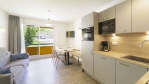 A modern kitchen with a dining area, a sofa, and a view of a green landscape. - Renovated studio in Gourette, 4 people, pets allowed, wifi (Gourette)