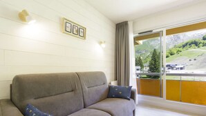 A modern living room with a grey sofa, two patterned cushions, a framed picture on the wall, and a large window with a view of a mountainous landscape. - Renovated studio in Gourette, 4 people, pets allowed, wifi (Gourette)
