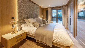 Una camera da letto moderna con un letto grande, pavimento in legno, un comodino e vista su un paesaggio innevato attraverso la finestra.