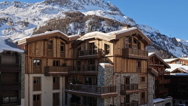 Un chalet in legno a più piani con balconi, dettagli in pietra e montagne sullo sfondo.
