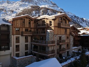 Un chalet en bois à plusieurs étages, doté de balcons, d’éléments décoratifs en pierre et surplombant un paysage montagneux.