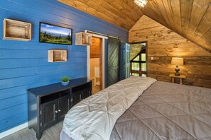 Une chambre avec un grand lit, un téléviseur fixé au mur et un plafond en bois.