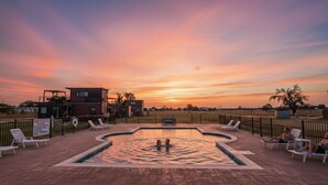 Piscina con sillas de descanso y un edificio al fondo durante el atardecer.