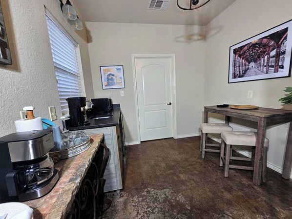 A compact kitchen with a coffee maker, a toaster, and a small dining table with two chairs.