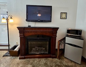 Una sala de estar con chimenea, televisor montado en la pared, microondas y lámpara.