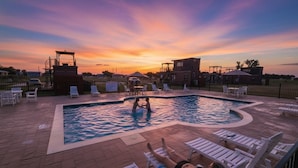 A swimming pool with lounge chairs and a lifeguard tower at sunset. - Wine Train Cottage · Hot Tub, Pool & Wine Trail (Fredericksburg)