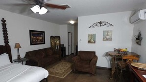 A room with a bed, two sofas, a dining table with chairs, a ceiling fan, and artwork on the walls. - Wine Train Cottage · Hot Tub, Pool & Wine Trail (Fredericksburg)