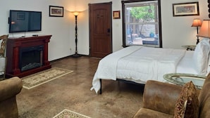 A bedroom with a bed, a television, a fireplace, and a window with blinds. - Wine Train Cottage · Hot Tub, Pool & Wine Trail (Fredericksburg)