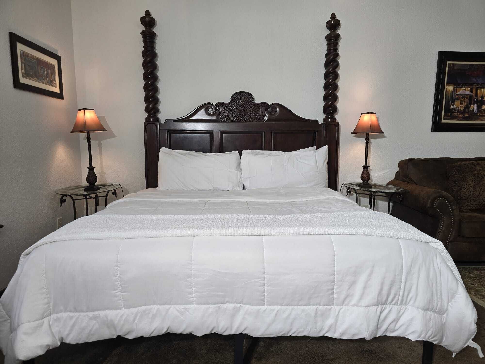 Ein Hotelzimmer mit einem Himmelsbett, weißer Bettwäsche, zwei Nachttischlampen und einem braunen Ledersofa.