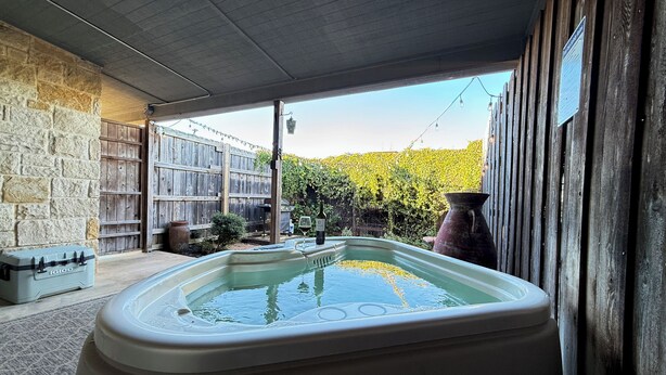 A hot tub in a covered outdoor area with stone walls and a wooden fence. - Wine Trail Cottage · Hot Tub, Pool & Wineries (Fredericksburg)