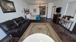 A living room with a black leather sofa, a round white coffee table, a patterned rug, and a staircase leading to an upper floor. - Wine Trail Cottage · Hot Tub, Pool & Wineries (Fredericksburg)